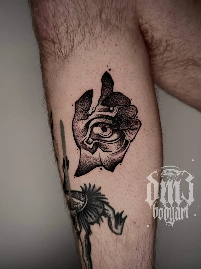 Stilisiertes Blackwork Tattoo einer abgehackten Hand mit einem strahlenden Augen-Motiv auf der Wade, gestochen im DM3 Bodyart Studio in Würzburg. Feine Linien, präzise Schattierungen und individueller illustrativer Stil im Dark-Art Look. Custom Tattoo mit einzigartigem Design für Tattoo-Liebhaber, die hochwertige Körperkunst suchen. Professionelles Tattoo-Studio in Würzburg – spezialisiert auf Blackwork, Dark-Art und illustrative Tattoos.