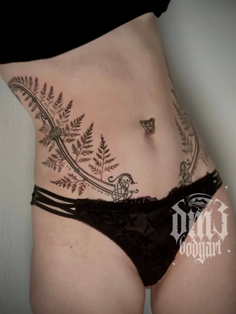 Detailreiches Black and Grey Tattoo eines kunstvollen Farns mit keltischen Knoten am Bauch, gestochen im DM3 Bodyart Studio in Würzburg. Feine Linien, präzise Schattierungen und individueller illustrativer Stil im Dark-Art Look. Custom Tattoo mit einzigartigem Design für Tattoo-Liebhaber, die hochwertige Körperkunst suchen. Professionelles Tattoo-Studio in Würzburg – spezialisiert auf Blackwork, Dark-Art und illustrative Tattoos.